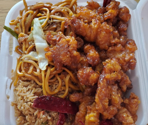 A takeout container with fried chicken in a sweet sauce, fried rice, and lo mein noodles with vegetables.