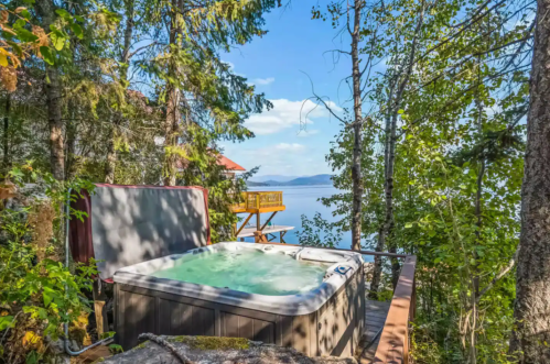 A hot tub surrounded by trees, overlooking a serene lake and blue sky.
