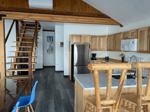 A modern kitchen with wooden cabinets, stainless steel appliances, and a staircase leading to an upper level.