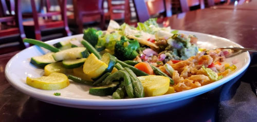 A plate of colorful vegetables including green beans, zucchini, broccoli, and a salad with guacamole.