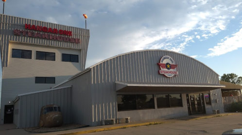 Exterior of Hangar One Steakhouse, featuring a modern building and a vintage airplane in front.