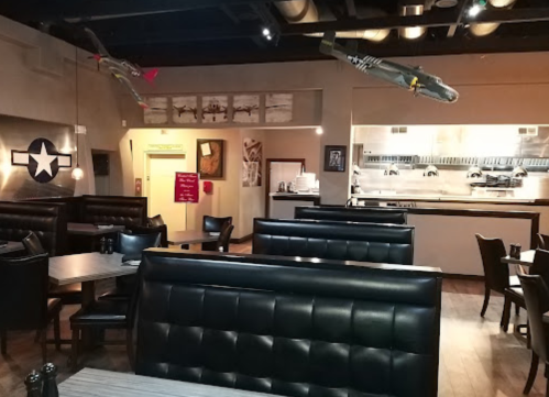 Interior of a restaurant featuring black booths, military-themed decor, and model airplanes hanging from the ceiling.