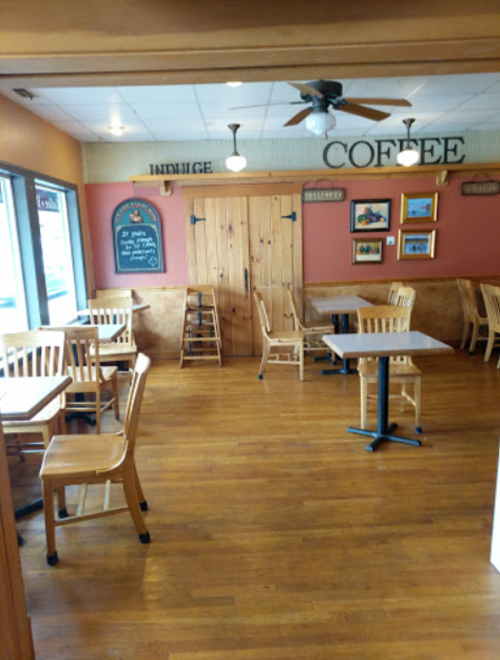 Cozy café interior with wooden tables and chairs, a chalkboard menu, and decorative wall art.