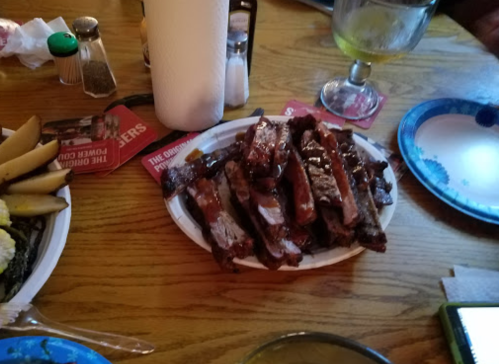 A plate of ribs sits on a wooden table, surrounded by condiments and side dishes.