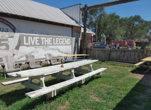 Outdoor seating area with picnic tables, a rustic backdrop, and a sign that reads "LIVE THE LEGEND."