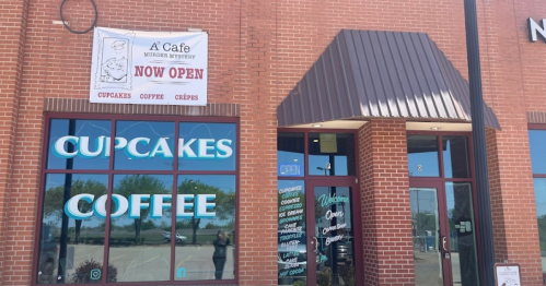 Exterior of a cafe with a sign reading "Now Open" and large windows displaying "Cupcakes" and "Coffee."