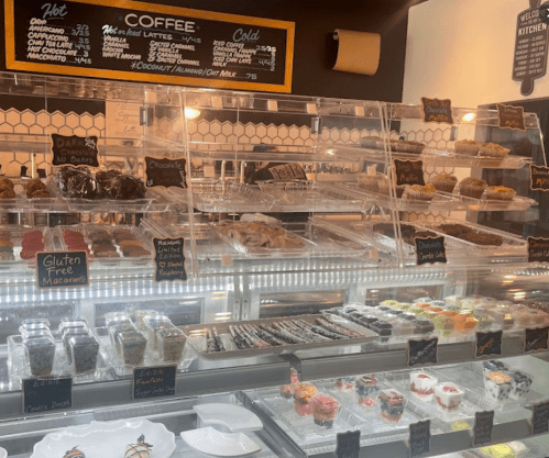 A display case filled with various pastries and desserts, alongside a chalkboard menu for coffee options.