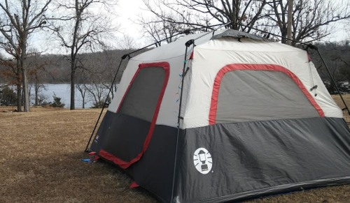 A large tent set up on grassy land near a lake, surrounded by bare trees and a clear sky.