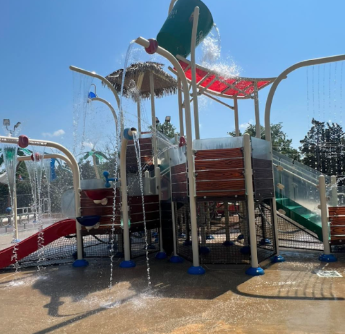 A colorful water play structure with slides and water features, surrounded by a sunny outdoor setting.