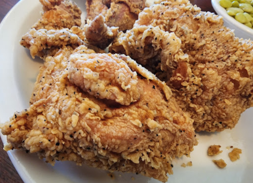 Close-up of crispy fried chicken pieces on a plate, with a side of green peas in the background.