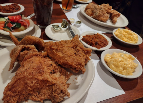 A table spread with fried chicken, macaroni and cheese, coleslaw, and drinks in a cozy restaurant setting.