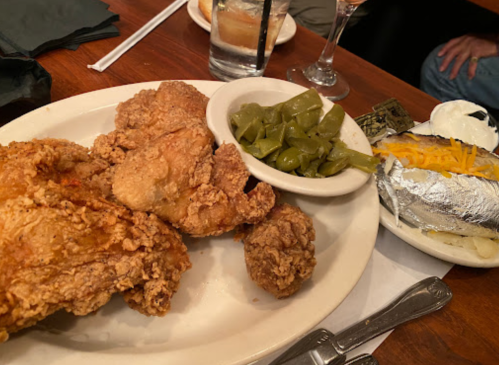 A plate of fried chicken with green beans and a baked potato topped with sour cream and cheese.