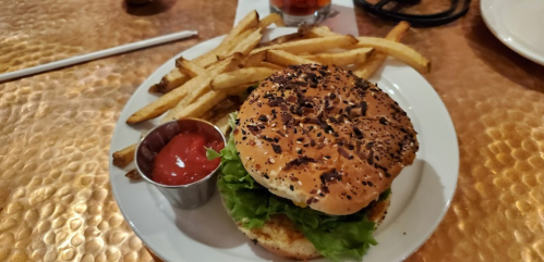 A plate with a sesame seed burger topped with lettuce and a side of golden fries and a small cup of ketchup.