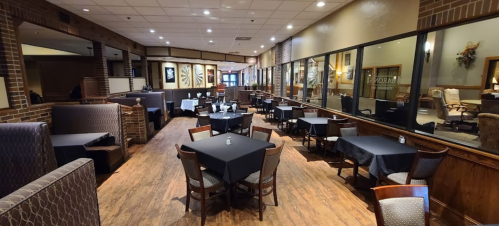 Interior of a restaurant featuring dark tables, booths, and large windows, creating a cozy dining atmosphere.