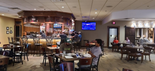 A restaurant interior with a bar, tables, and patrons dining. A TV displays a sports game in the background.
