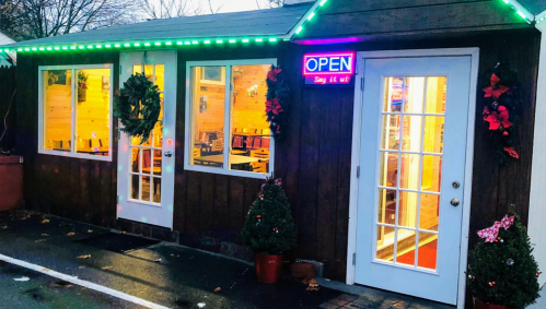 A cozy building decorated with wreaths and lights, featuring an "OPEN" sign and warm interior lighting.