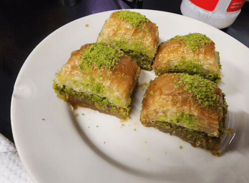 A plate of four pieces of baklava topped with crushed pistachios, showcasing layers of flaky pastry and nuts.