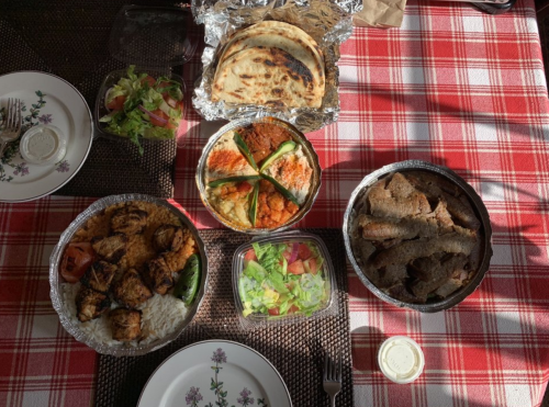 A table set with a checkered cloth featuring various dishes: grilled meat, rice, salad, and flatbreads.