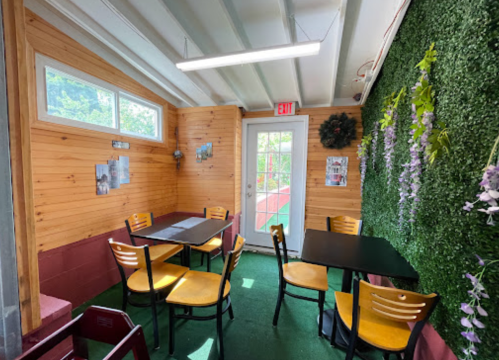 Cozy indoor seating area with wooden walls, green plants, and tables set for dining. Bright and inviting atmosphere.