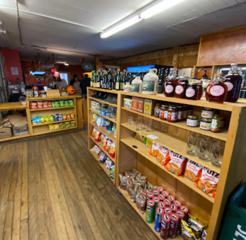 A wooden shelf filled with snacks, drinks, and jars in a cozy store with a rustic interior.
