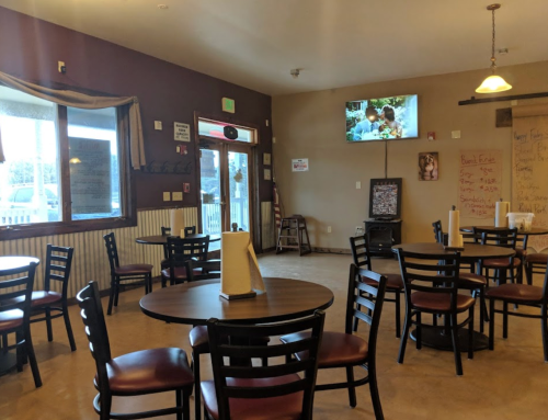 Interior of a casual dining restaurant with empty tables, chairs, and a TV showing a scene on the wall.