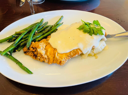 A plate featuring fried chicken topped with creamy sauce, served with green beans on the side.