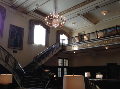 Elegant interior of a grand lobby featuring a chandelier, staircase, and large windows with draped curtains.