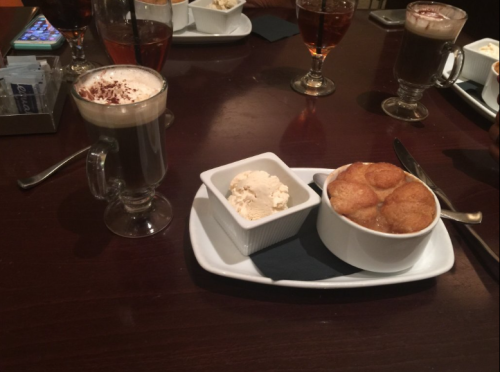 A dessert plate with a warm pastry and a scoop of ice cream, alongside a glass of coffee on a wooden table.