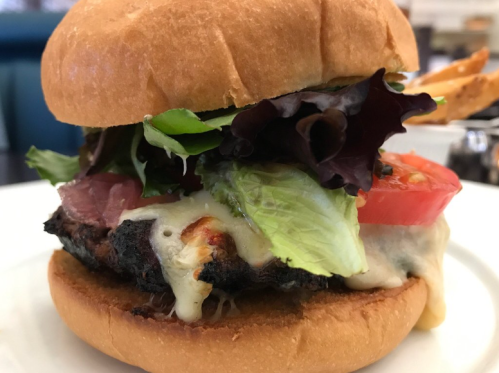 Close-up of a burger with melted cheese, lettuce, tomato, and a toasted bun, served with fries on the side.