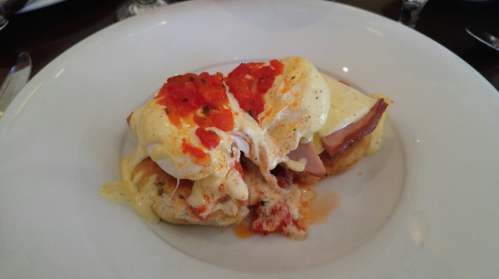 A plate of eggs Benedict with poached eggs, ham, and a creamy sauce, topped with red pepper flakes.