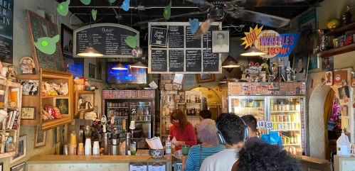 A cozy café interior with a colorful menu board, vintage decor, and customers ordering at the counter.