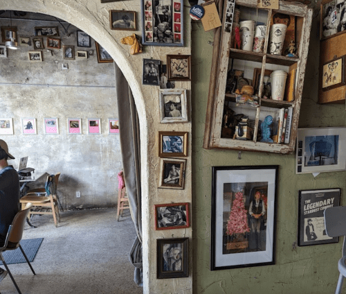 A cozy café interior with an archway, walls adorned with framed photos and eclectic decor, and a glimpse of patrons.