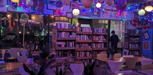Cozy café interior with bookshelves, colorful lights, and plants, creating a warm, inviting atmosphere.