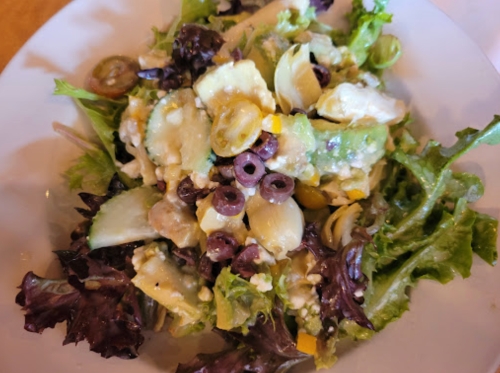 A fresh salad with mixed greens, artichokes, olives, and diced vegetables in a light dressing.