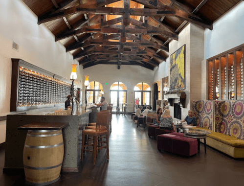 A spacious restaurant interior with high ceilings, wooden beams, a bar, and colorful seating areas.