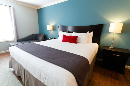 A cozy hotel room featuring a large bed, a nightstand, a lamp, and a seating area with a blue wall backdrop.