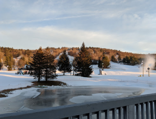A snowy landscape with ski slopes, trees, and a frozen pond under a clear sky.