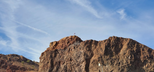 A rocky mountain peak under a blue sky with wispy clouds, featuring a bird perched on top.