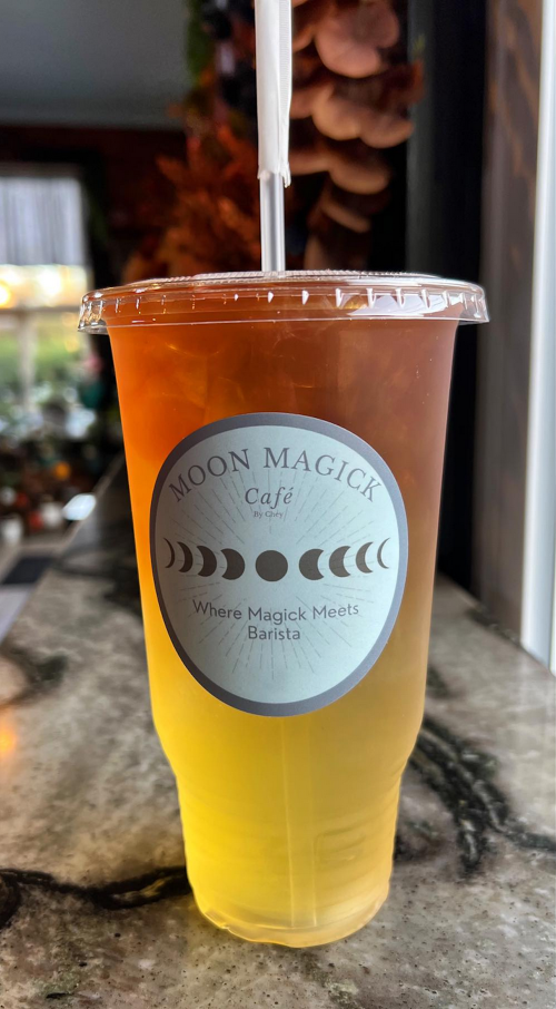 A clear cup filled with a layered drink, featuring a label that reads "Moon Magick Café" on a marble countertop.