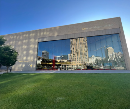 Reflection of a modern building, Maurice Abravanel Hall, on glass, surrounded by green grass and trees.