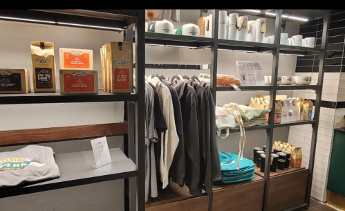 Merchandise display featuring clothing, mugs, and snacks on shelves in a modern retail space.
