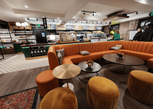 Cozy café interior featuring orange seating, round tables, and a counter with pastries and drinks. Warm, inviting atmosphere.