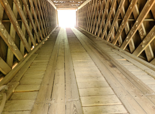 View looking up a wooden ramp or tunnel, leading to a bright light at the end.