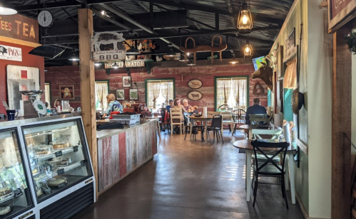 A cozy restaurant interior with wooden decor, tables, and a display case, featuring patrons enjoying their meals.