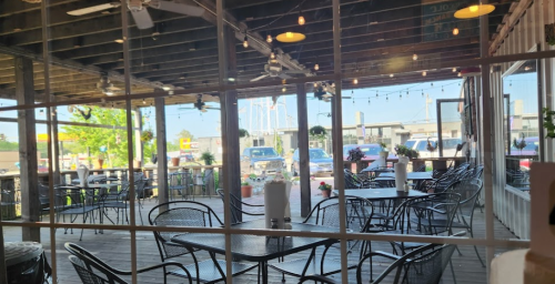 A view of a restaurant patio with empty tables and chairs, surrounded by large windows and string lights.