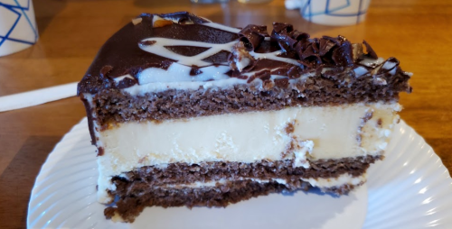 A slice of chocolate cake with layers of cream filling, topped with chocolate shavings and decorative icing.