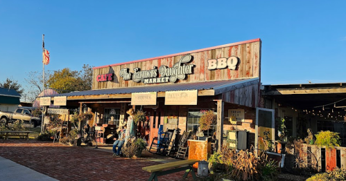 A rustic market building with a sign reading "The Famous Daughter Market" and BBQ, surrounded by outdoor seating.
