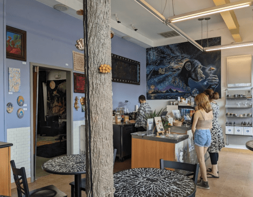 A cozy café interior with a mural, a barista serving customers, and artistic decor on the walls.