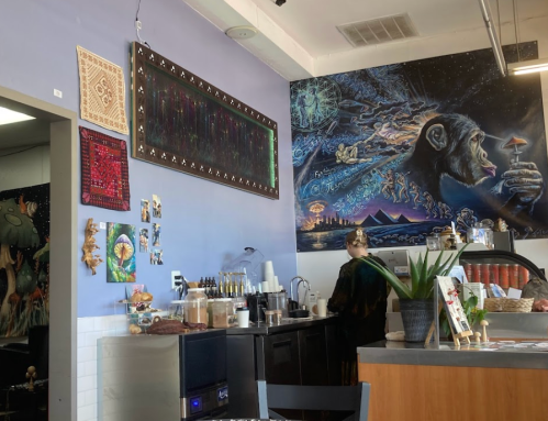 A cozy café interior featuring a colorful mural, a barista at work, and various art pieces on the walls.