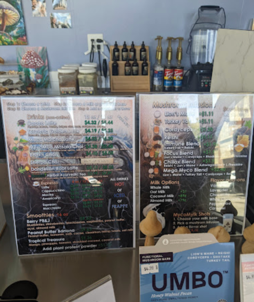 Menu board displaying drinks, smoothies, and mushroom blends at a café, with prices and options listed.